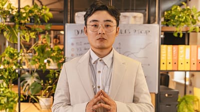 Jeune professionnel se tenant confiant dans un bureau avec de la verdure et un tableau de récapitulatif des ventes.