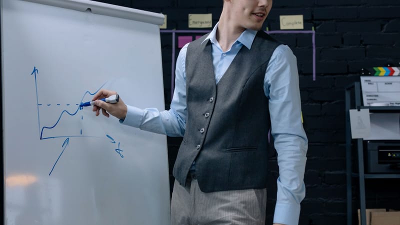 Un homme d'affaires dessinant un graphique sur un tableau blanc lors d'une présentation dans un environnement de bureau.
