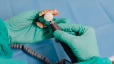 Gros plan sur un technicien dentaire polissant une prothèse avec des outils de précision et des gants chirurgicaux.