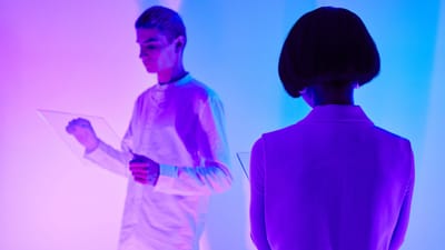 Deux personnes interagissent avec des interfaces numériques dans un environnement futuriste coloré.