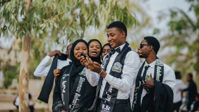 Un groupe de diplômés célébrant en plein air, capturant des moments joyeux sur un smartphone.