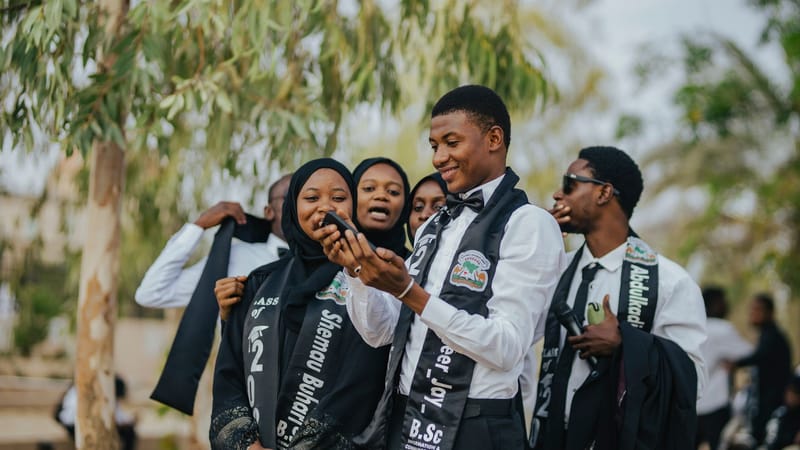 Un groupe de diplômés célébrant en plein air, capturant des moments joyeux sur un smartphone.