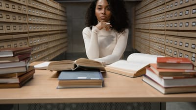 Femme afro-américaine étudiant avec des livres dans une zone d'archives de bibliothèque.