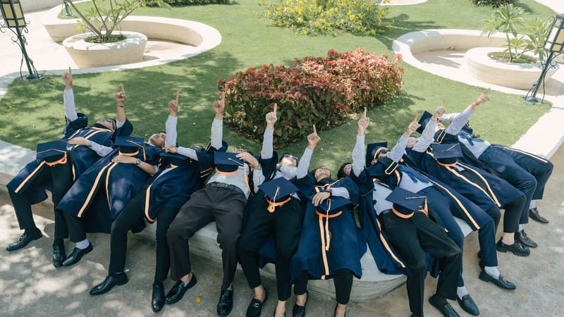 Par une journée ensoleillée, les diplômés, coiffés de leurs toques et de leurs robes, célèbrent leur réussite en pointant le ciel du doigt.