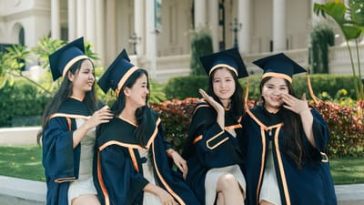 Un groupe de quatre jeunes diplômées, rayonnantes de bonheur, célèbrent ensemble en toge et en chapeau de diplômée, en plein air.