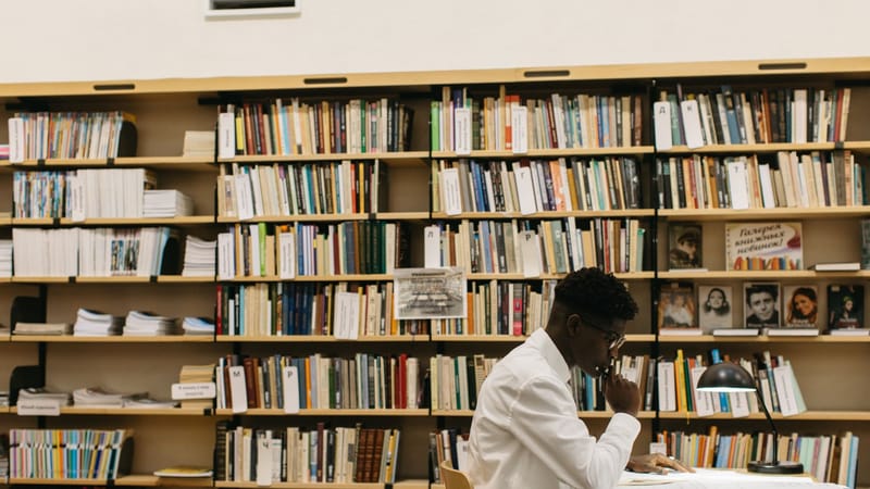 Un homme étudiant avec attention dans une bibliothèque remplie d'étagères de livres, créant une atmosphère réfléchie.