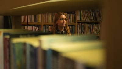 Jeune femme dans une bibliothèque regardant pensivement les étagères de livres.
