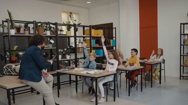 Des étudiants participent activement en levant la main dans une salle de classe moderne avec un enseignant attentif et un environnement organisé.