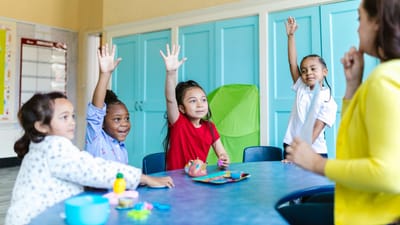 Enfants levant les mains avec enthousiasme dans une salle de classe colorée, engagés dans l'apprentissage.