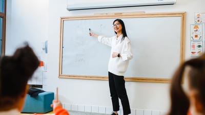 Professeur souriant instructant des élèves dans une salle de classe avec un tableau blanc.