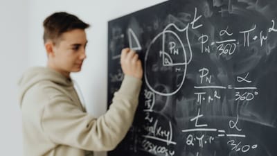 Adolescent concentré résolvant une équation mathématique sur un tableau noir dans une salle de classe.
