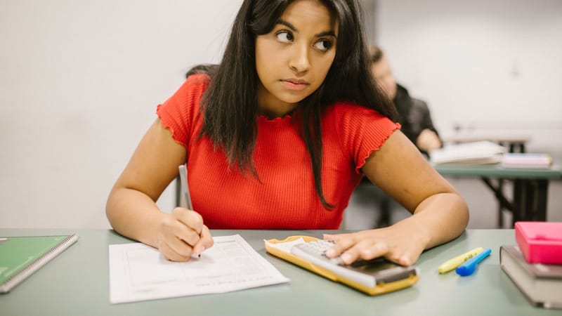 Étudiant concentré en chemise rouge utilisant une calculatrice pendant un examen en classe.