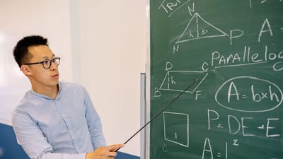 Professeur de mathématiques démontrant des équations au tableau dans une salle de classe.