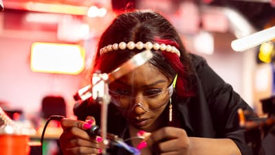 Femme réparant intensément des appareils électroniques avec des outils de précision et un fer à souder à l'intérieur.