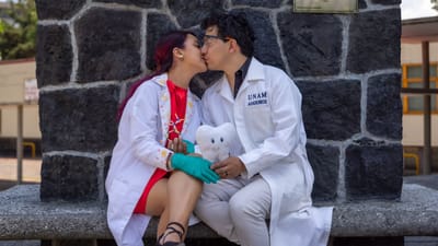 Un jeune couple en blouses blanches partage un moment romantique près d'un monument en pierre à l'extérieur.