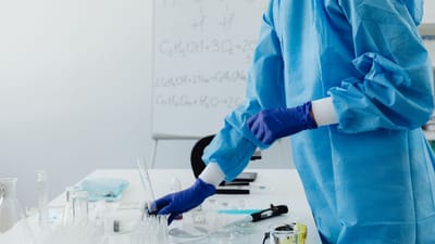 Scientifique en vêtements de protection travaillant dans un laboratoire avec des formules chimiques sur un tableau blanc.