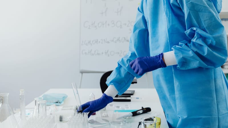 Scientifique en vêtements de protection travaillant dans un laboratoire avec des formules chimiques sur un tableau blanc.