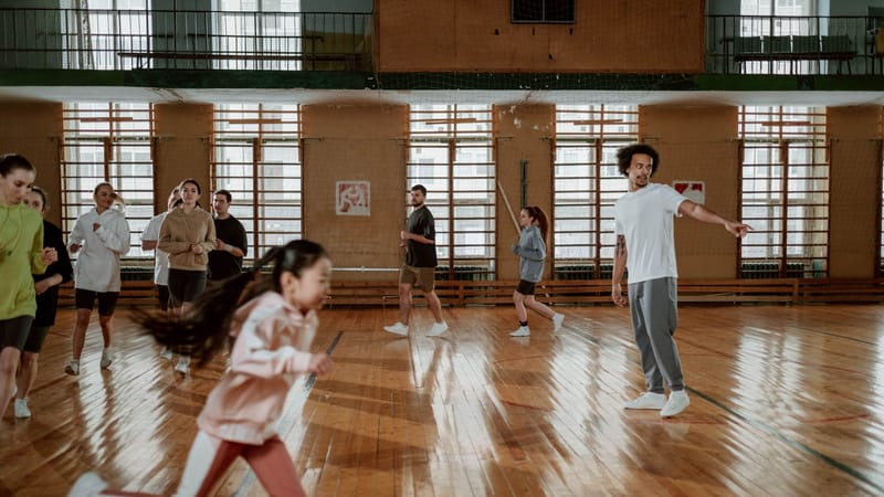 Un groupe diversifié de personnes courant et s'entraînant sur un terrain de basketball intérieur avec un sol en bois.