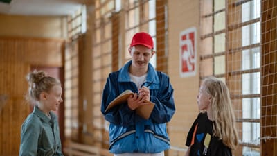 Un entraîneur masculin interagit avec deux filles lors d'une activité sportive dans un gymnase intérieur.
