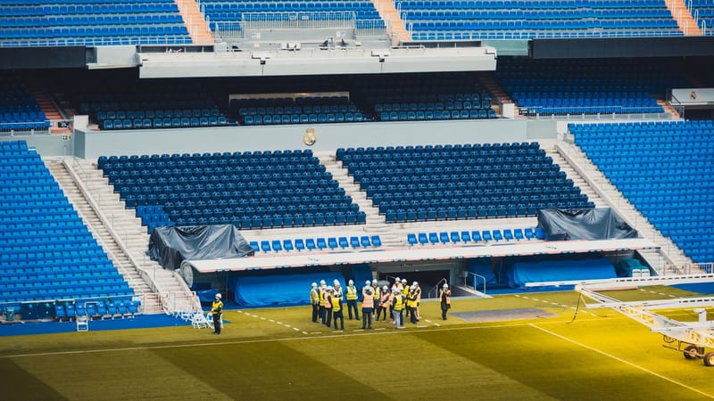 Une vue en grand angle d'une zone de sièges dans un stade à Madrid avec des travailleurs visibles et des sièges bleus vibrants.