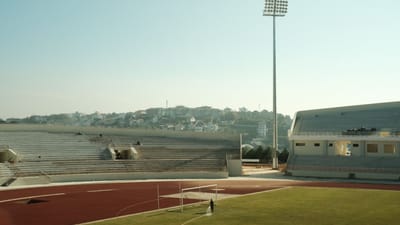 Vue large d'un stade de sport extérieur avec des sièges vides et un terrain sous un ciel bleu clair.
