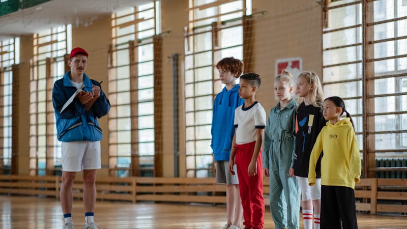 Un entraîneur instruisant un groupe diversifié d'enfants pendant un cours de gym dans un hall sportif scolaire.
