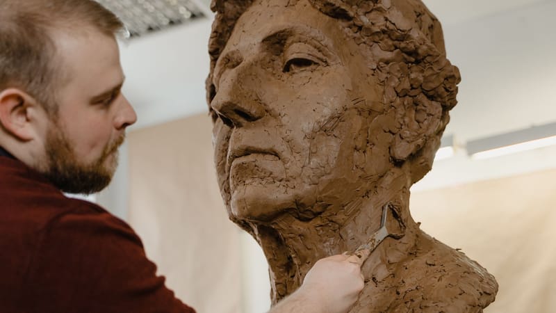 Gros plan d'un sculpteur façonnant méticuleusement un buste en argile avec un outil de boucle dans un studio.
