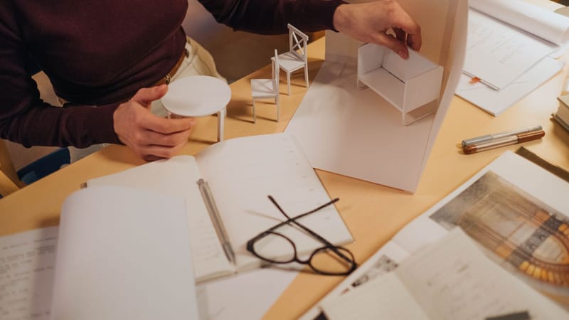 Architecte travaillant sur des modèles de meubles miniatures dans un espace créatif. Accent sur le processus de design fait main.