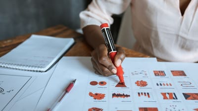 Gros plan sur une personne marquant des graphiques d'affaires avec un marqueur rouge, illustrant l'analyse de données et la planification.