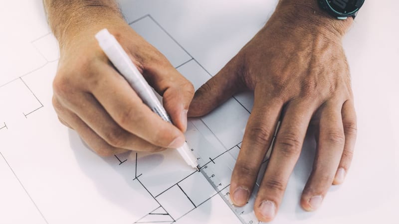Mains esquissant des plans architecturaux avec précision à l'aide d'une règle et d'un stylo sur papier.