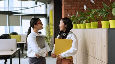 Deux jeunes professionnelles engagées dans une conversation dans un bureau moderne.