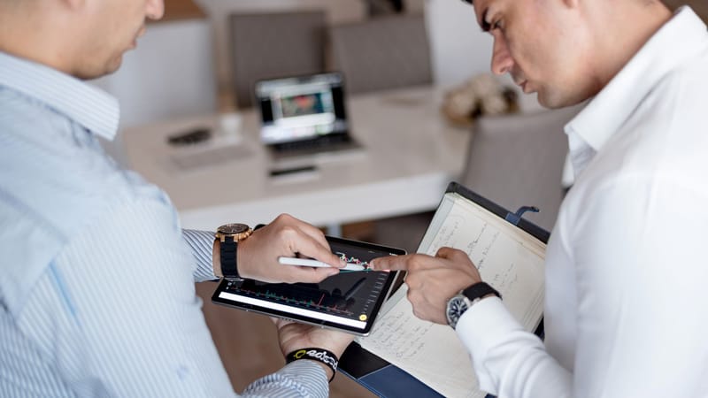 Deux professionnels examinant des graphiques financiers sur une tablette lors d'une réunion d'affaires.
