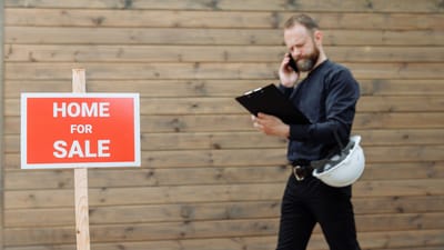 Un agent immobilier au téléphone avec un panneau 'Maison à vendre' devant une propriété.
