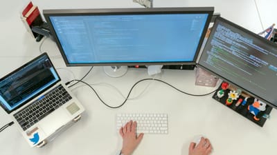 Une ingénieure logicielle féminine codant sur des double écrans et un ordinateur portable dans un bureau.