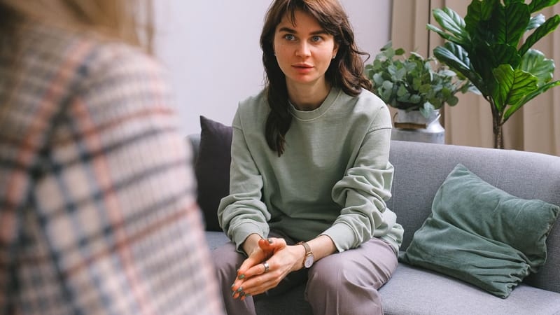 Une femme concentrée lors d'une séance de thérapie, assise sur un canapé à l'intérieur.