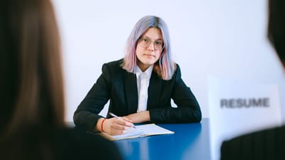 Une jeune femme aux cheveux teints prend des notes lors d'un entretien d'embauche.