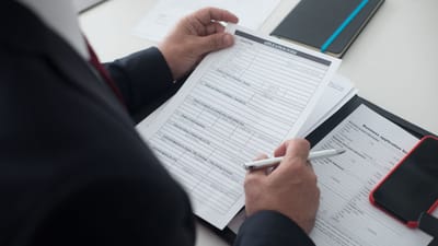 Un homme d'affaires en costume noir consulte un formulaire de candidature imprimé avec un stylo sur son bureau.