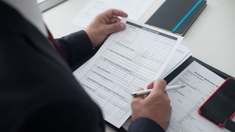 Un homme d'affaires en costume noir consulte un formulaire de candidature imprimé avec un stylo sur son bureau.