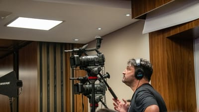 Un caméraman manipule des caméras vidéo professionnelles lors d'un événement en intérieur. Idéal pour les thématiques liées aux médias et à la diffusion.