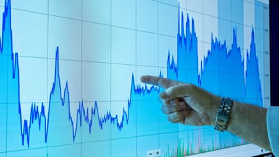 Une main désigne un graphique financier sur un grand écran, indiquant les tendances du marché.