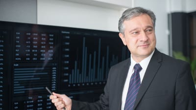 Homme professionnel en costume examinant des graphiques financiers sur un moniteur, présentant les tendances du marché boursier.