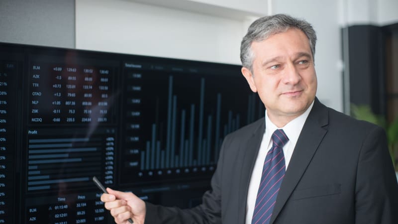 Homme professionnel en costume examinant des graphiques financiers sur un moniteur, présentant les tendances du marché boursier.