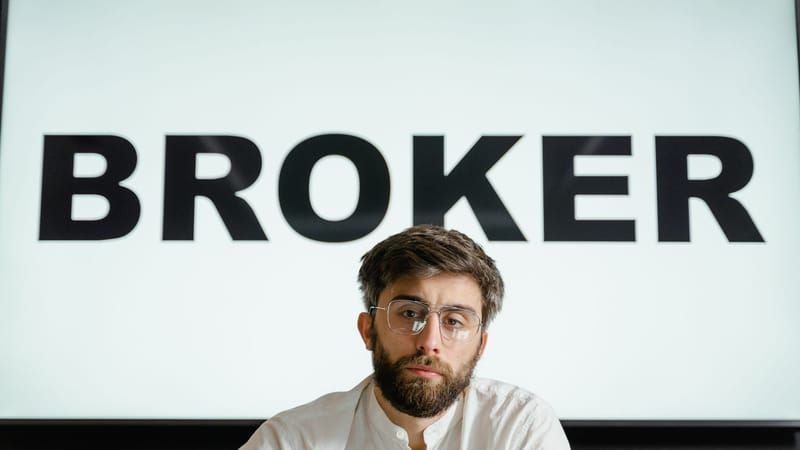 Portrait d'un homme d'affaires confiant assis dans un bureau sous le panneau 'BROKER'.