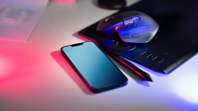 Espace de travail moderne avec une tablette à stylet, un smartphone et une souris d'ordinateur sous un éclairage coloré.