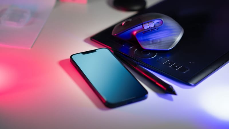 Espace de travail moderne avec une tablette à stylet, un smartphone et une souris d'ordinateur sous un éclairage coloré.