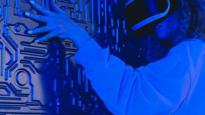 Une femme portant un casque VR touche un mur texturé dans un environnement futuriste éclairé de bleu.