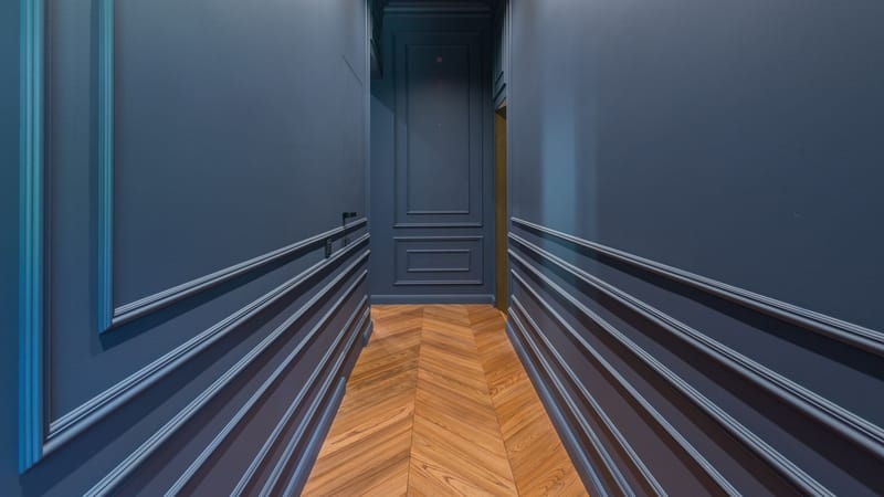 Un couloir élégant avec des murs bleus et un sol en bois au motif en chevrons.