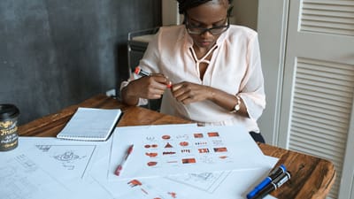 Femme africaine avec des dreadlocks travaillant sur des diagrammes à un bureau, portant des lunettes et une blouse.