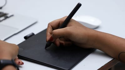 Gros plan sur des mains utilisant une tablette graphique avec un stylet pour un design créatif, prise à Chennai, Inde.