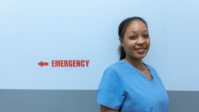 Travailleuse de la santé heureuse en tenue de soin se tenant près du panneau de salle d'urgence.